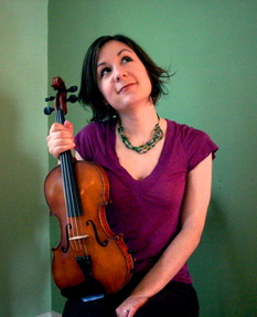 a white woman with dark hair and a magenta shirt, looking up and to the side and holding a fiddle