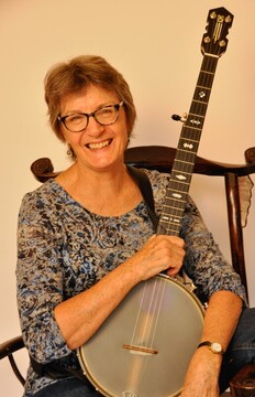 a white middle aged woman with glasses and short red hair holding a banjo and smiling