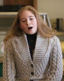 a young white woman with long blond hair singing, wearing a cream cable knit sweater