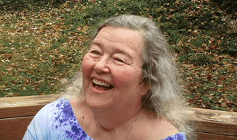 a white woman with long grey hair and a wrinkled face looking up and smiling