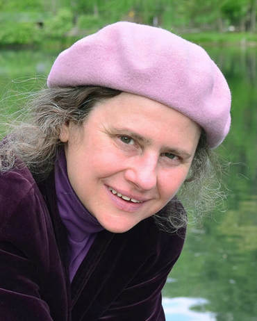 a white woman with grey hair and a pink hat looking at the camera and smiling
